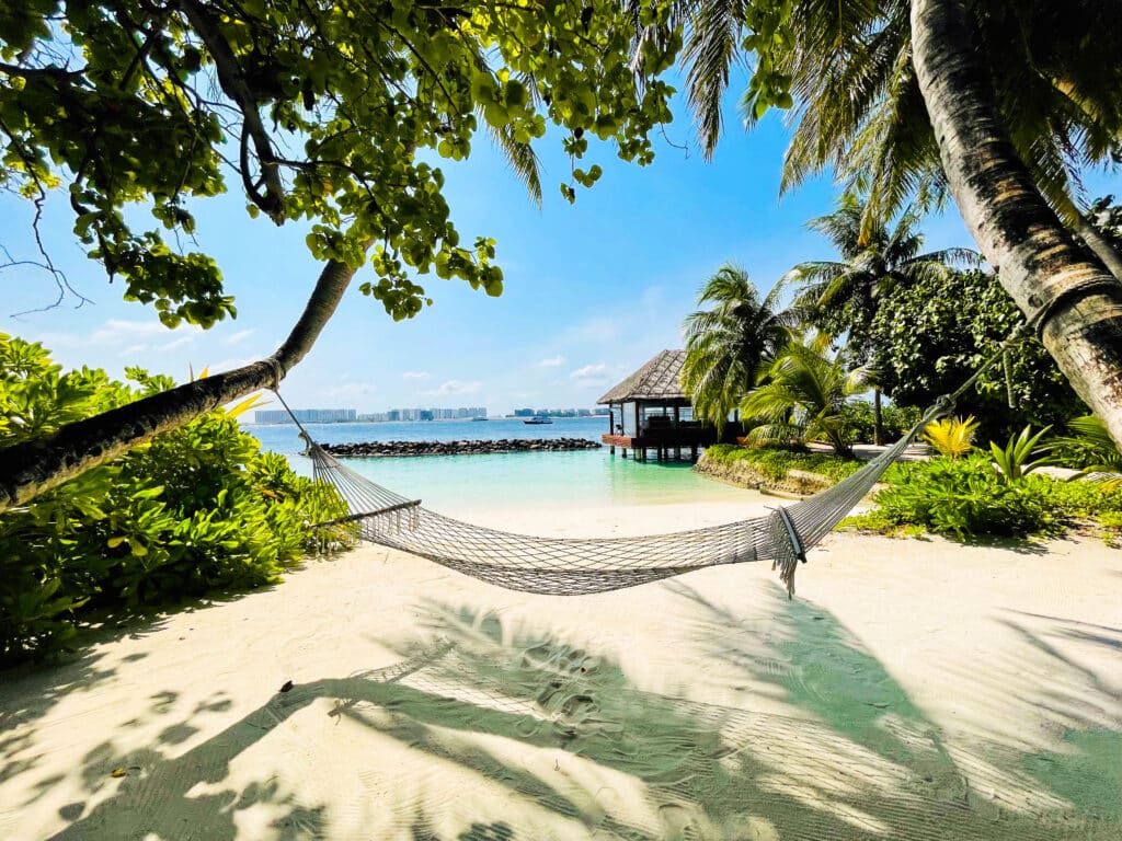 Shaded beach hammock strung between palm trees overlooking the turquoise lagoon at Hard Rock Hotel Maldives.