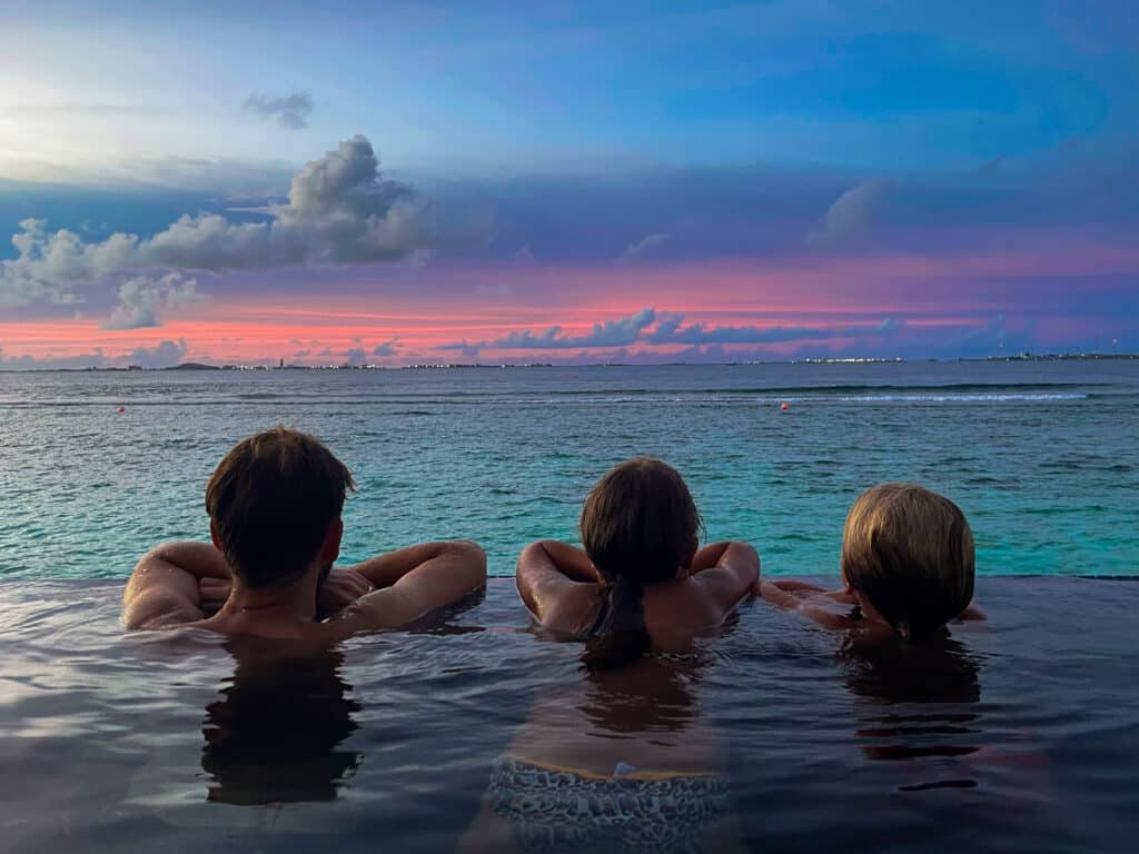 Family relaxing together in a private infinity pool at sunset overlooking the lagoon at Hard Rock Hotel Maldives.