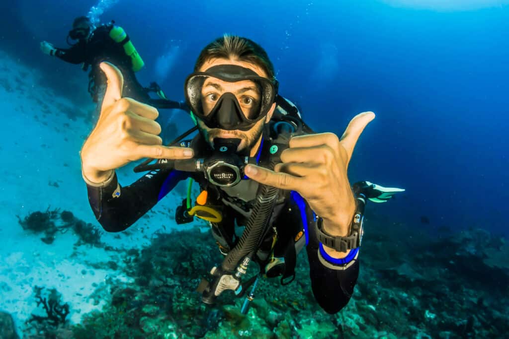 Happy Scuba Diver dando una señal de mano sobre el arrecife en uno de los principales sitios de buceo de la Guía de buceo de Maldivas.