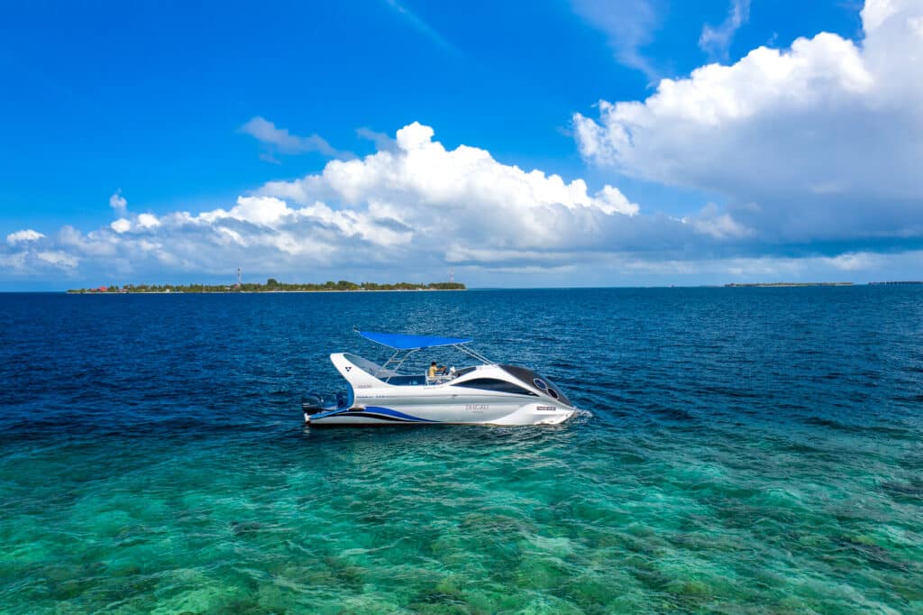 Sleek white speedboat floating over clear blue Maldivian water near a small island.
