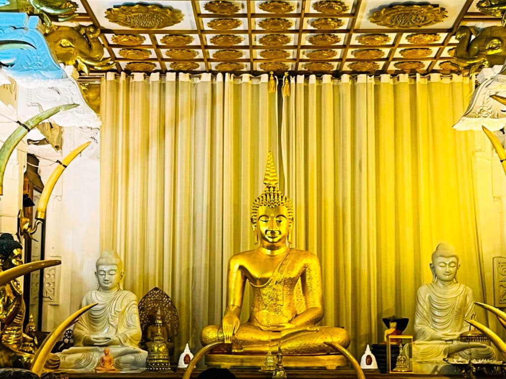 Золотые статуи Будды и белые фигуры святилищ внутри Храма Зуба Будды в Канди.