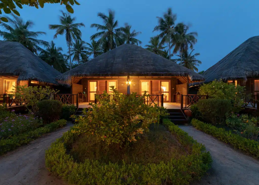 Los mejores resorts económicos en Maldivas: 10 opciones asequibles 3 villas de jardín con techo de paja brillando al atardecer entre palmeras y vegetación tropical