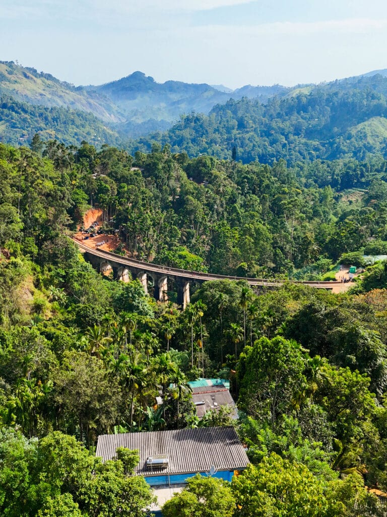 Drone view of Sri Lanka’s Nine Arches Bridge curving through dense tropical forest.