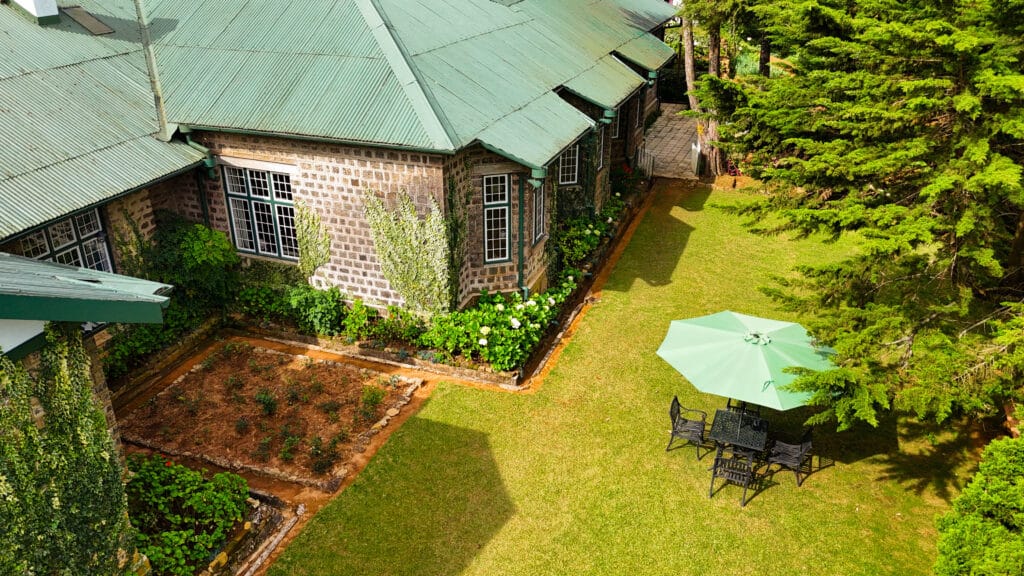 Aerial view of a colonial‑style guesthouse with green roof and garden in Sri Lanka’s hills.