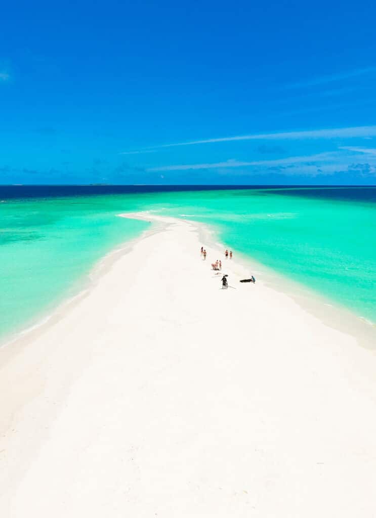 Wide tropical beach with turquoise lagoon and lush greenery under a blue sky in the sandbank Maldives.