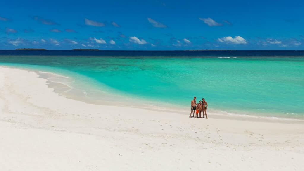 Family standing on a wide white sandbank surrounded by bright turquoise sea in the local islands in Maldives.