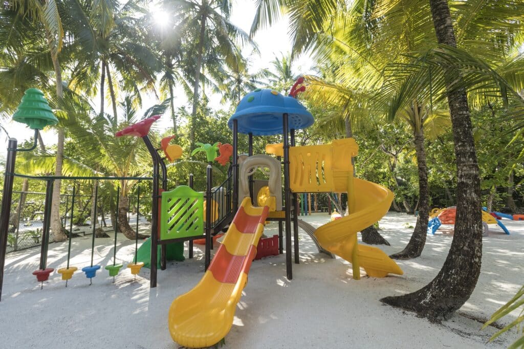 Colorful playground with slides and climbing structures shaded by palm trees.