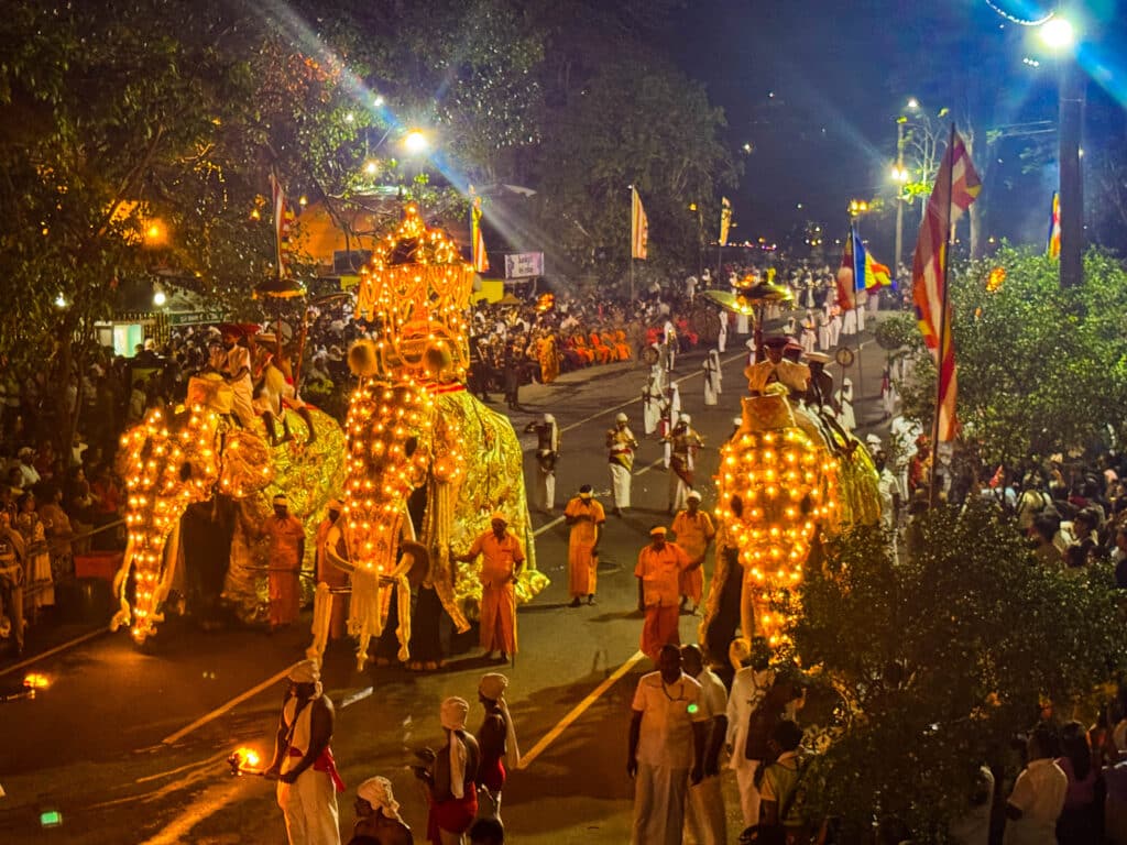 Nighttime procession of illuminated elephants and performers fills a busy street during a grand Sri Lankan festival.