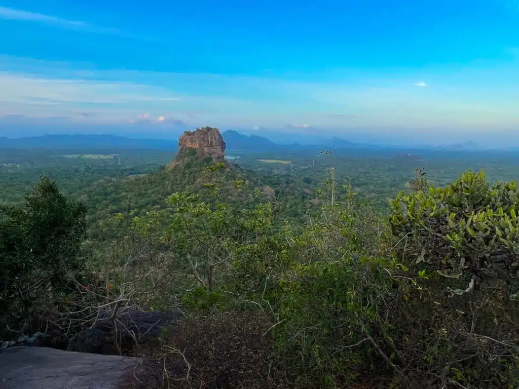 إطلالة بانورامية على صخرة Sigiriya وهي ترتفع فوق الغابة الخضراء المورقة تحت سماء صافية خلال أفضل وقت لزيارة سريلانكا من حيث الطقس.
