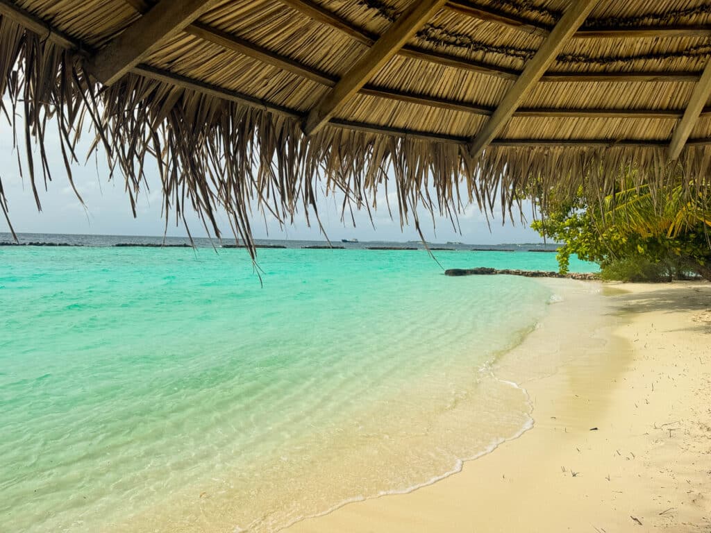 Laguna tranquila con agua turquesa y arena suave sombreada por una choza de playa de paja en las Maldivas.