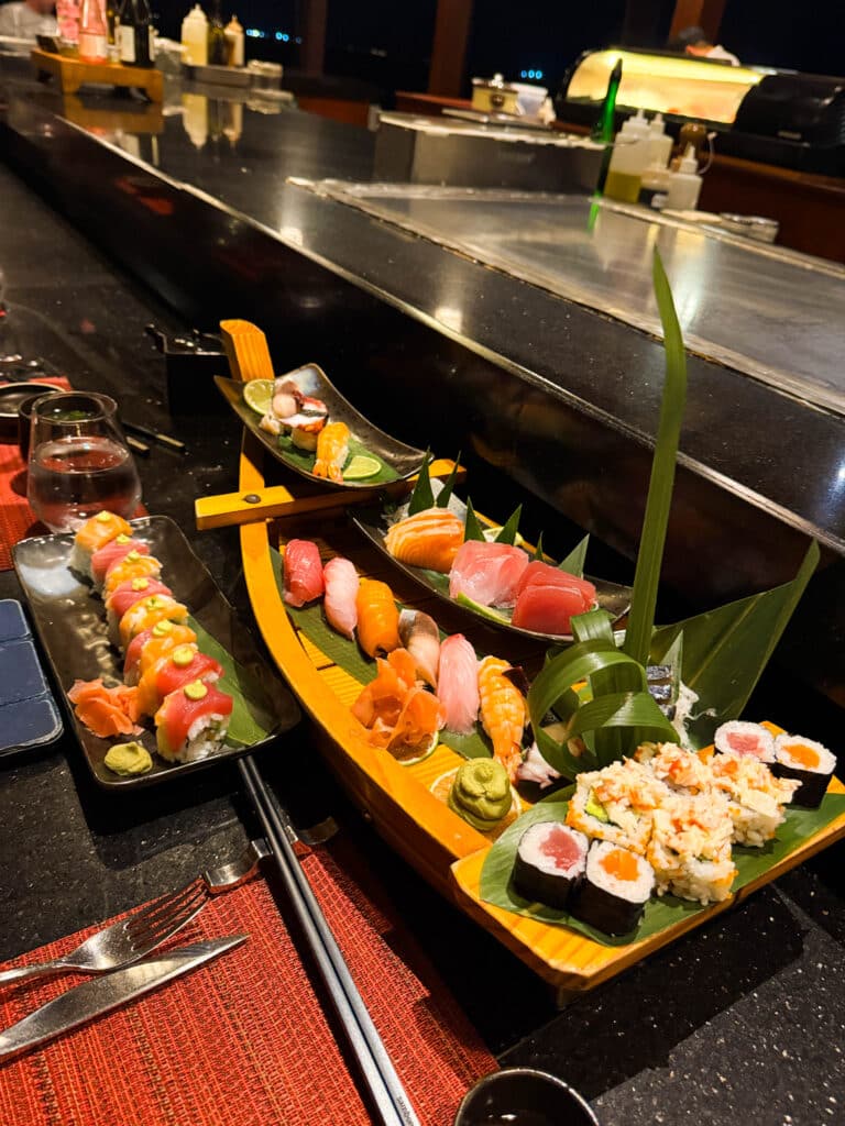 Colorful sushi and sashimi platters arranged on wooden boats at a resort restaurant.