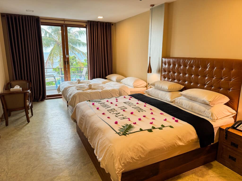 Spacious family room at Kiha Beach with a large double bed, extra beds, and balcony doors facing the sea.