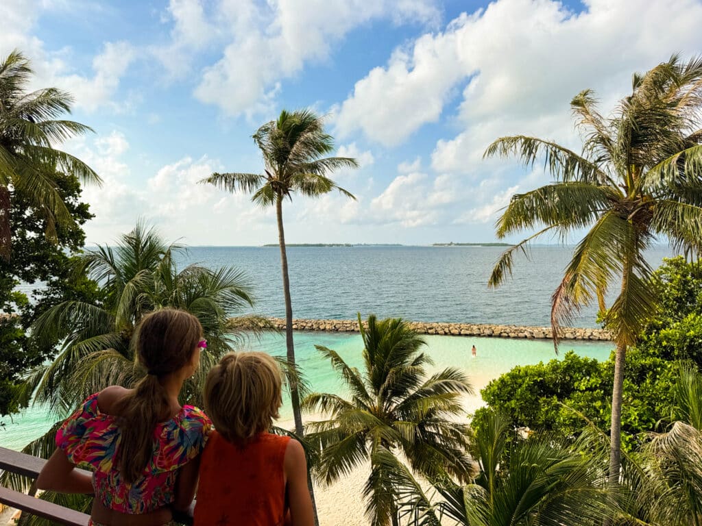 Dos niños mirando sobre las palmeras y una playa de bikini protegida desde el balcón de una casa de huéspedes.