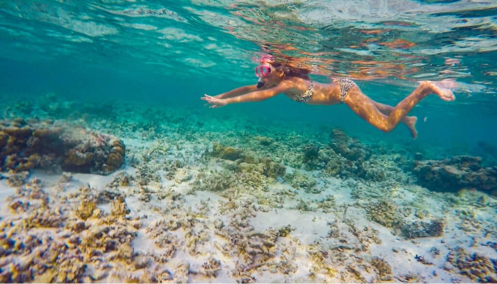 Woman snorkeling over a shallow coral reef near a sandy beach on a Maldivian local island.