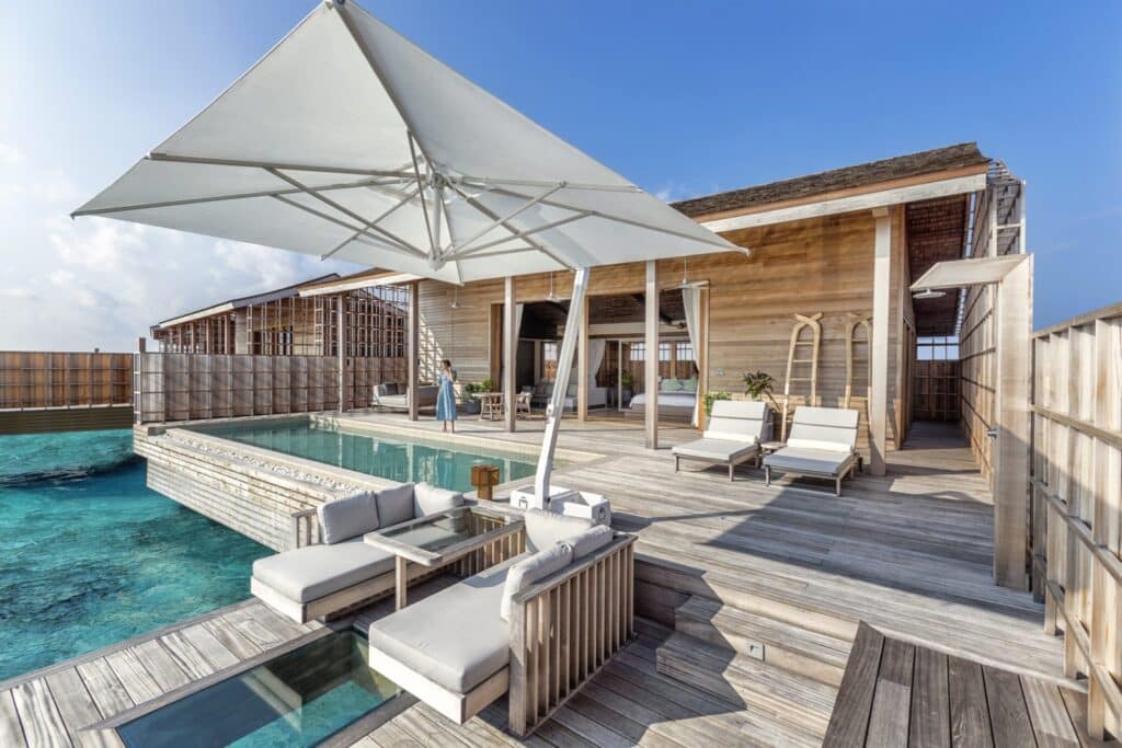 Spacious wooden overwater deck with sun loungers, umbrella, and private infinity pool.