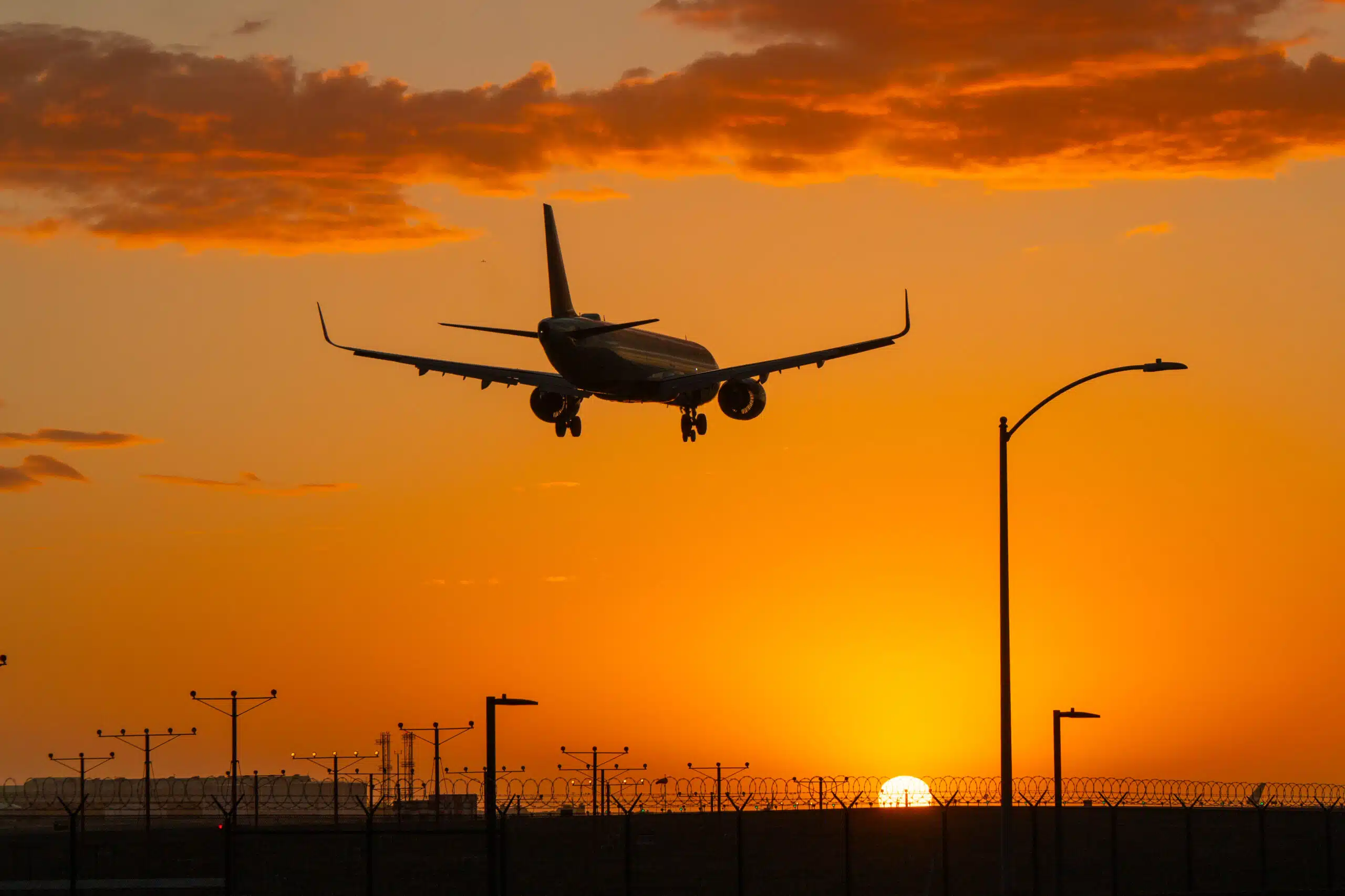 Airplane silhouette landing against a vivid orange sunset sky.