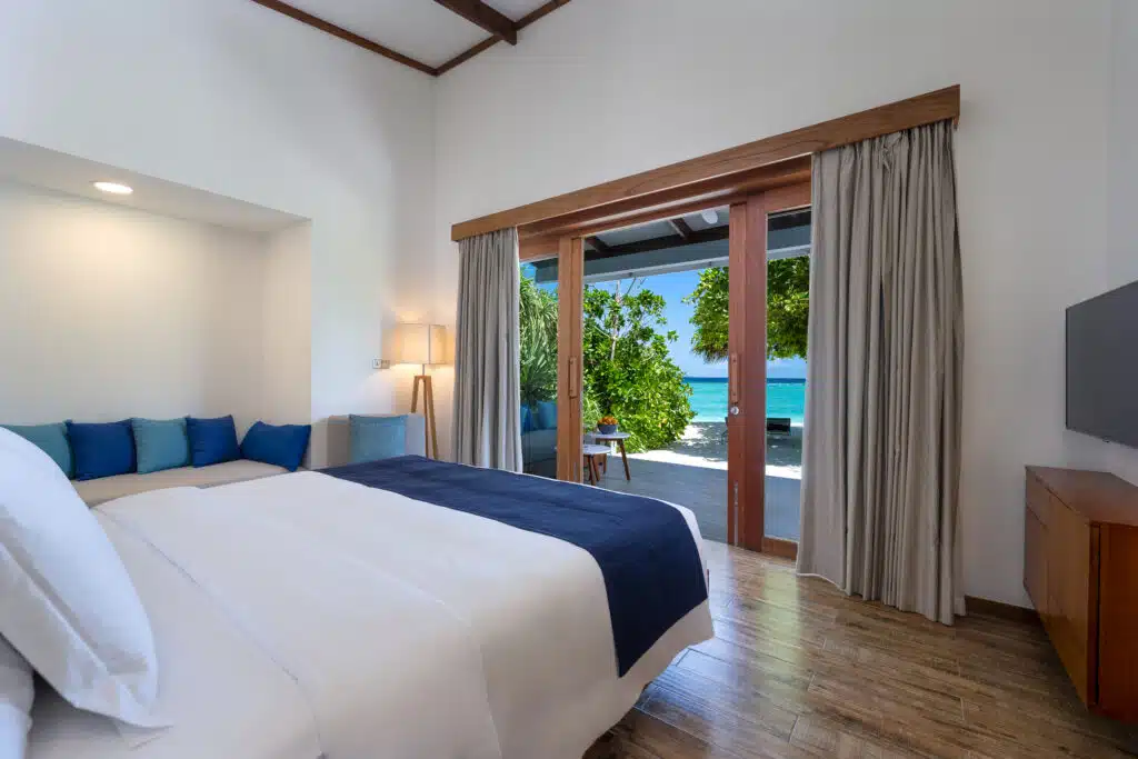 Los mejores resorts económicos en Maldivas: 10 opciones asequibles 10 luminoso dormitorio de villa de playa con puertas correderas abiertas que enmarcan la vegetación y el mar turquesa