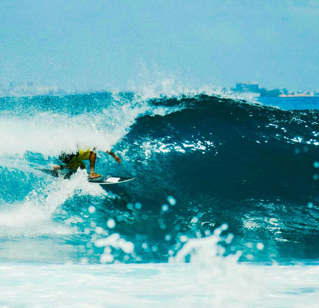 Surfer riding a powerful turquoise wave at a Maldivian surf break