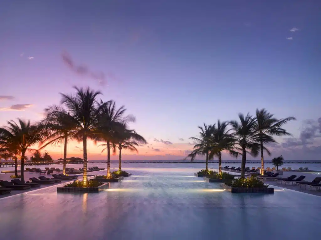 Los mejores resorts económicos en Maldivas: 10 opciones asequibles 8 gran piscina infinita del resort rodeada de palmeras iluminadas al atardecer con vistas al océano