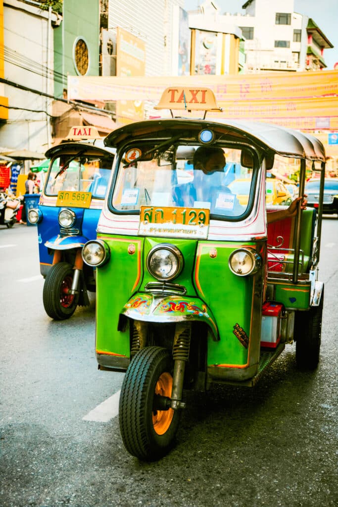 Green and blue tuk‑tuk taxis driving through a busy Asian city street.