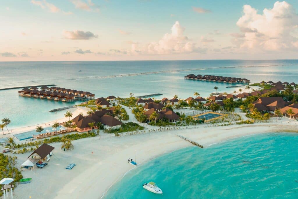 Vista aérea de un resort en una isla maldiva con villas sobre el agua y playas de arena blanca.