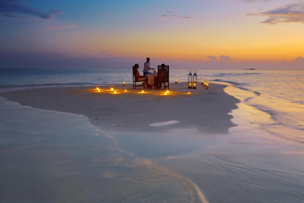 Romántica cena privada en un banco de arena al atardecer durante un viaje a las Maldivas.