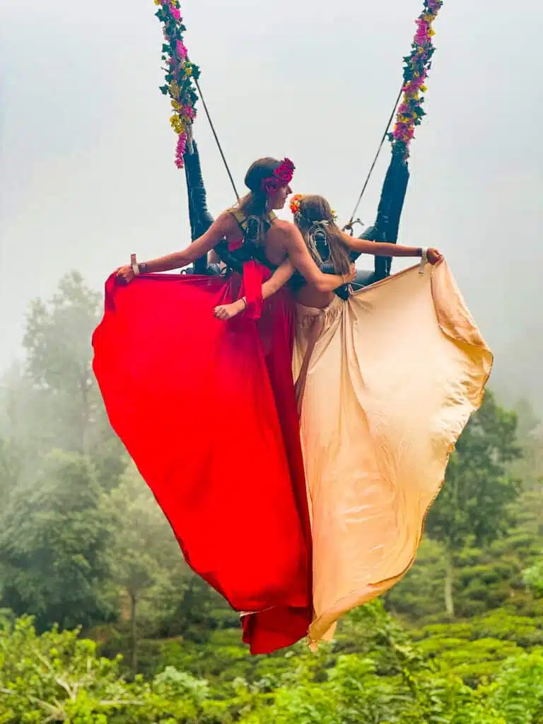 Le migliori cose da fare in Sri Lanka: le esperienze più gratificanti sull'isola 20 Due donne con abiti fluidi color crema e rosso sull'altalena panoramica di Flying Ravana sopra le piantagioni di tè nella nebbia di Ella