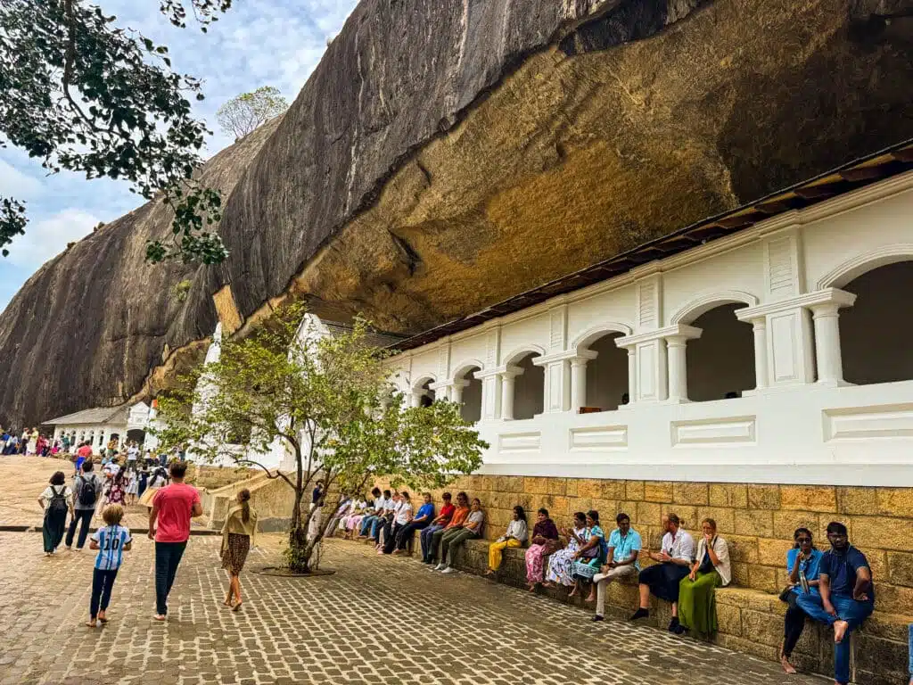Le migliori cose da fare in Sri Lanka: le esperienze più gratificanti sull'isola 22 Visitatori che camminano lungo la terrazza di fronte al bianco Dambulla Cave Temple scavato nella parete rocciosa in Sri Lanka