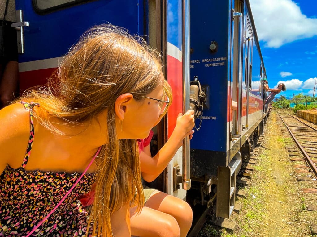 Itinerario di 7 giorni in Sri Lanka: Kandy, la regione collinare e la costa 4 ragazza che si sporge dalla porta blu di un treno in Sri Lanka guardando il paesaggio scorrere sulla tratta da Kandy a Ella