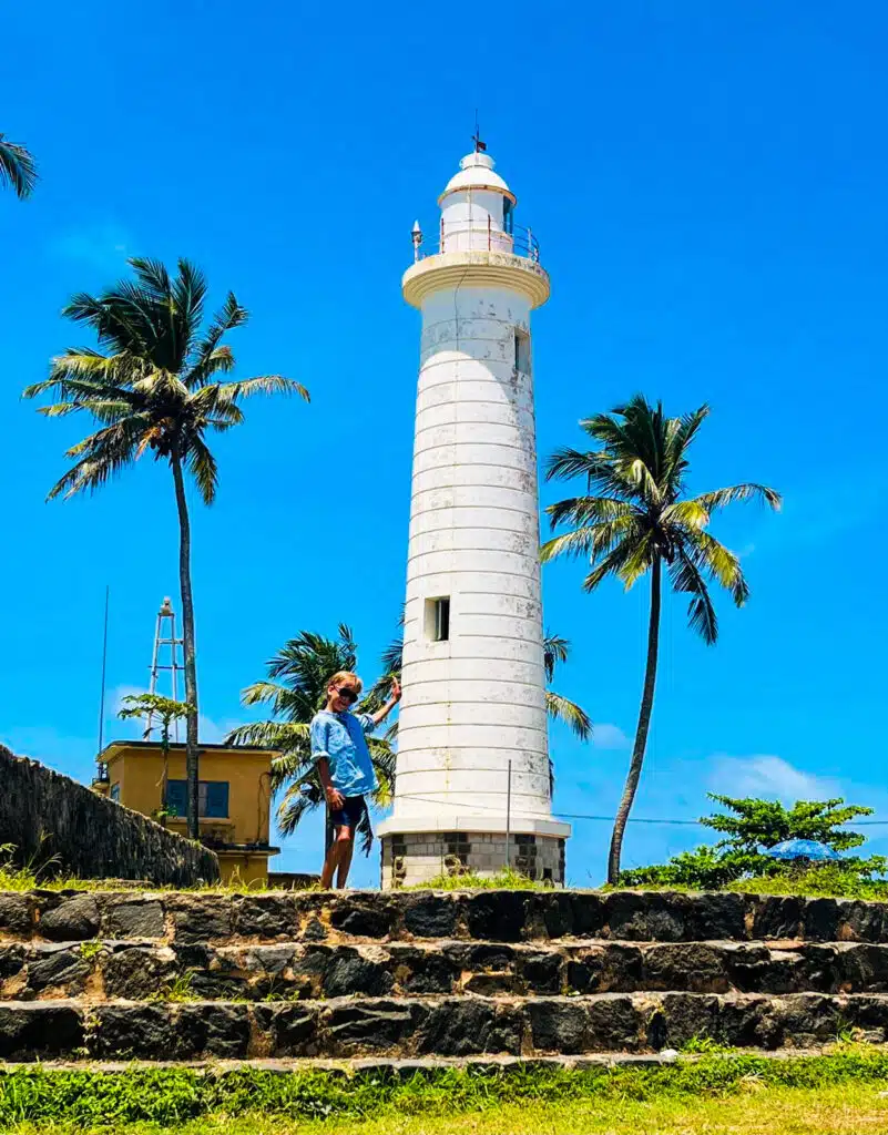 Le migliori cose da fare in Sri Lanka: le esperienze più gratificanti sull'isola 13 Bambino in piedi accanto al faro bianco di Galle Fort con palme contro un cielo azzurro brillante in Sri Lanka