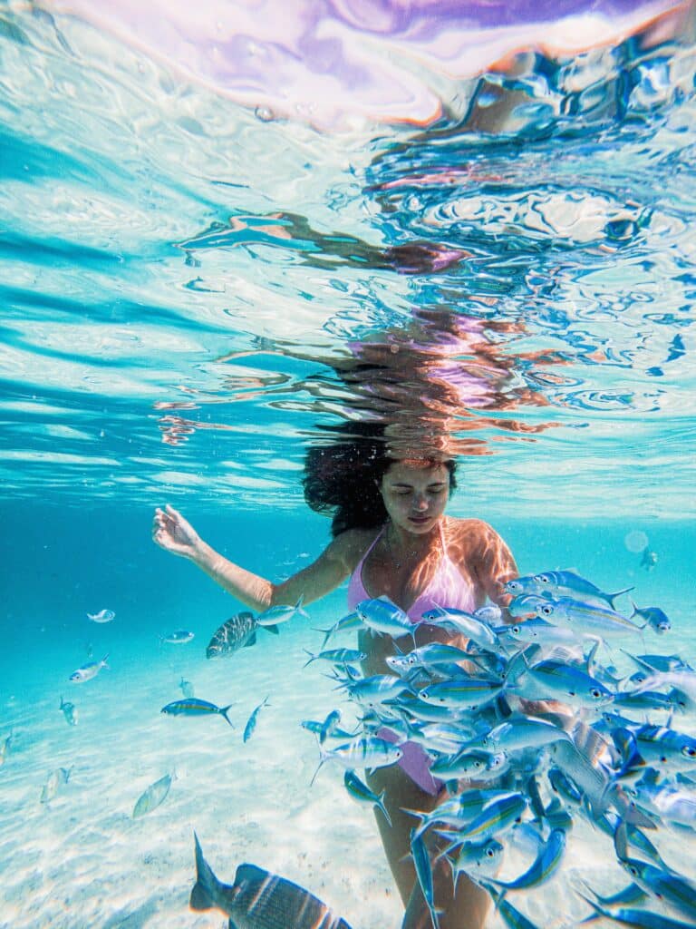 浅いモルディブ ラグーンで魚の群れに囲まれた水中を泳いでいる女性
