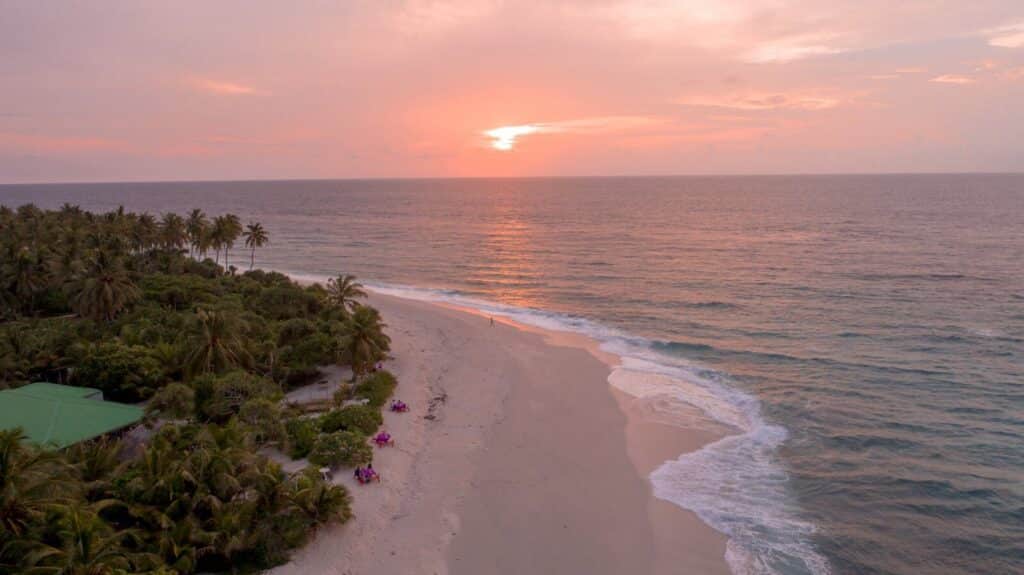 tramonto rosa sulla spiaggia dell'isola locale di Dhiffushi con oceano calmo e palme Maldive