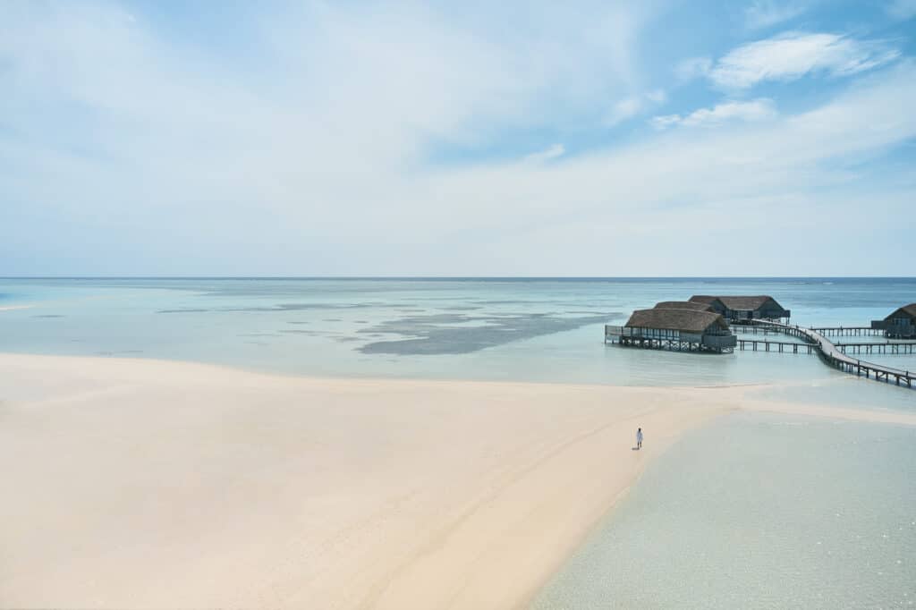 lone person walking on vast white sandbank at Como Cocoa Island Maldives with overwater villas