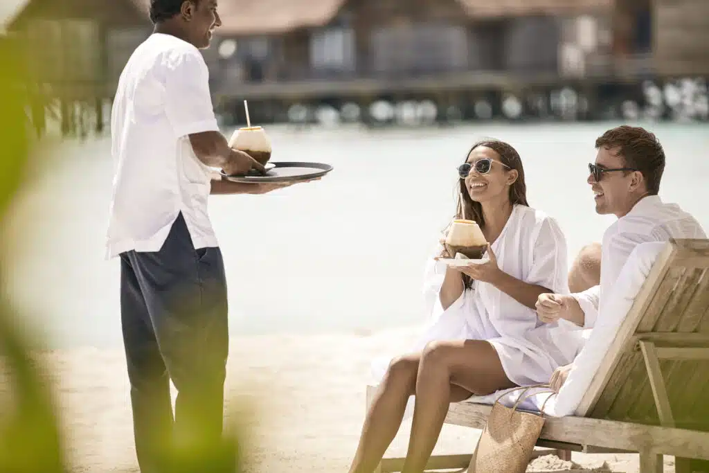 I migliori resort alle Maldive vicino a Malé: 10 isole top vicine all'aeroporto 17 coppia sulla spiaggia di COMO Cocoa Island mentre si gode il servizio di cocco sulla sabbia bianca