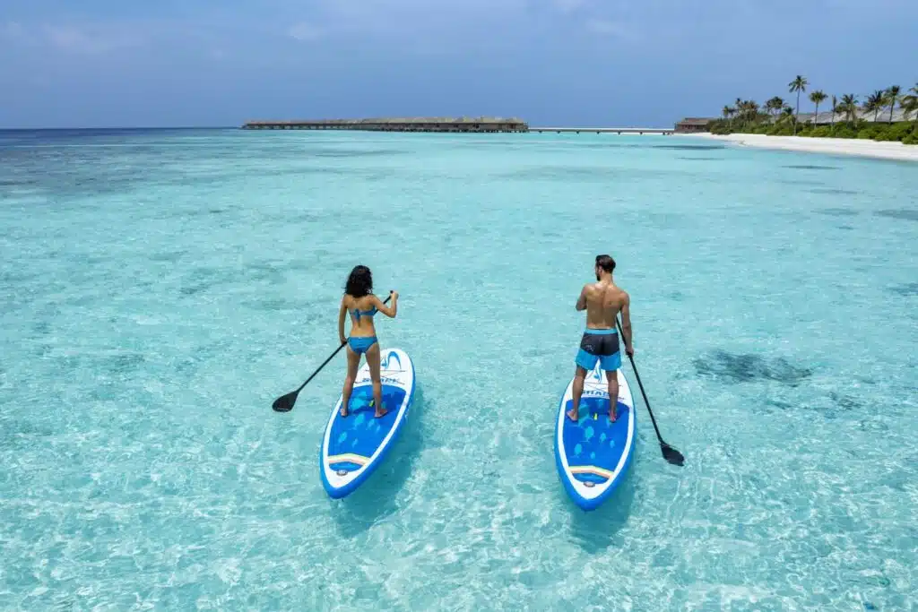 How to Choose a Maldives Resort: The Complete Decision Guide 8 couple stand up paddleboarding in crystal clear turquoise lagoon at Hurawalhi Island Resort Maldives