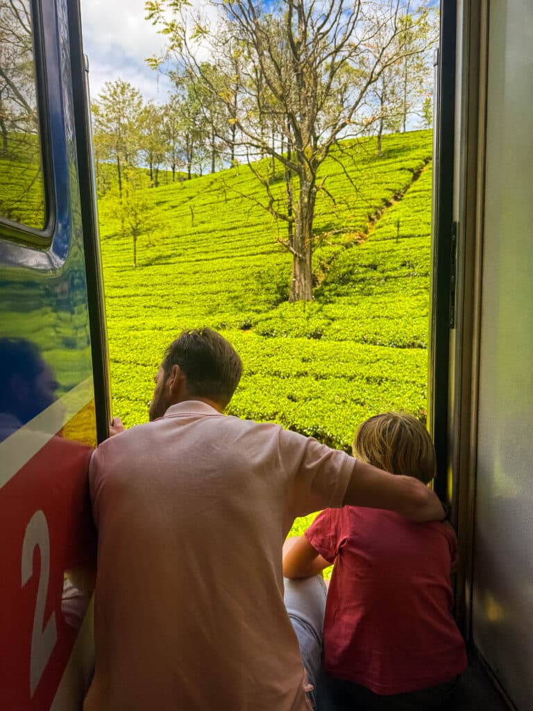 padre e figlio che si sporgono dalla porta del treno con vista sulle colline verdeggianti delle piantagioni di tè in Sri Lanka