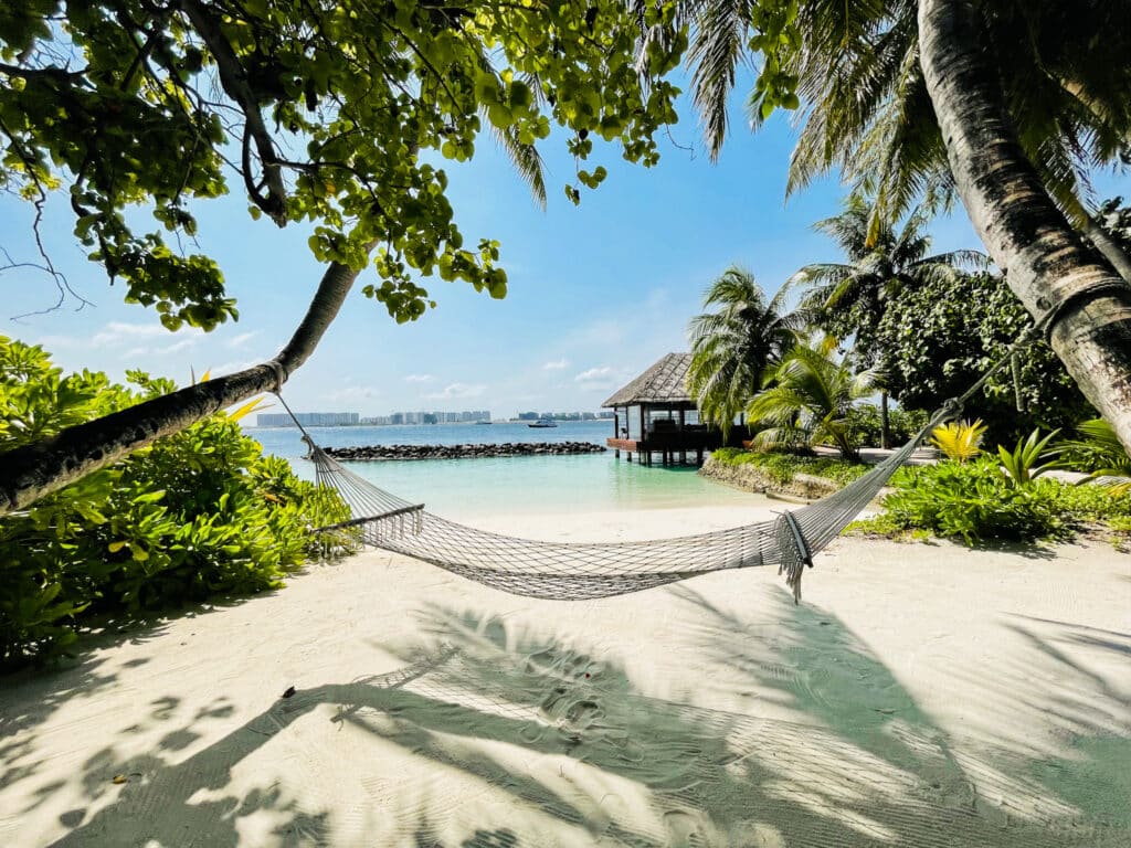 How to Choose a Maldives Resort: The Complete Decision Guide 3 hammock between palm trees on white sand beach at Kurumba Maldives with lagoon and overwater pavilion