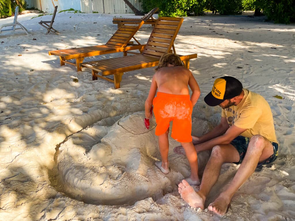 Maldive con bambini: resort o isole locali — Qual è la scelta giusta per la tua famiglia? 23 Famiglie che passeggiano lungo la spiaggia sabbiosa dell'isola di Dharavandhoo, nel Baa Atoll