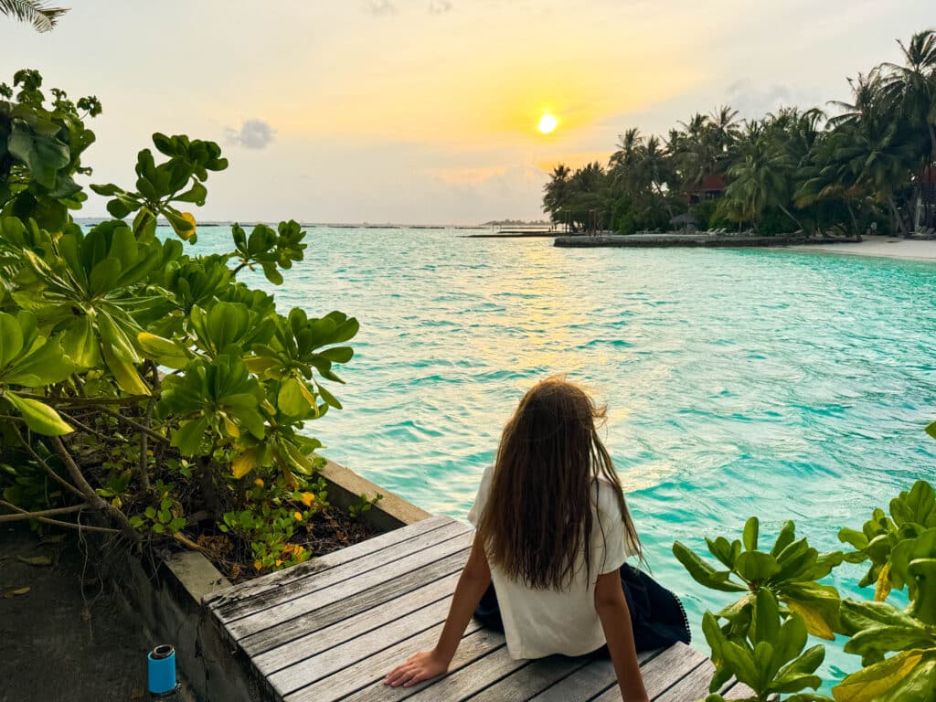 Los mejores resorts de Maldivas con mejor relación calidad-precio: 10 islas privadas que superan su precio 7 chica sentada en un embarcadero de madera observando el atardecer sobre la laguna turquesa en Kurumba Maldives