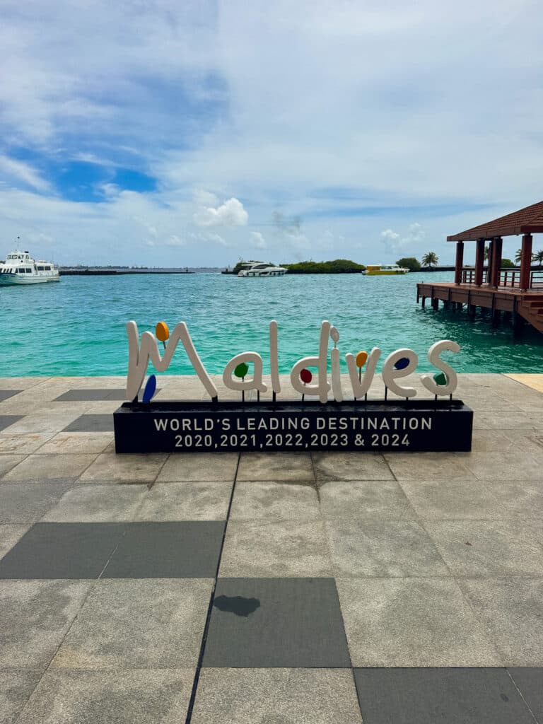 Insegna della destinazione leader al mondo alle Maldive sul lungomare di Malé con laguna turchese e barche