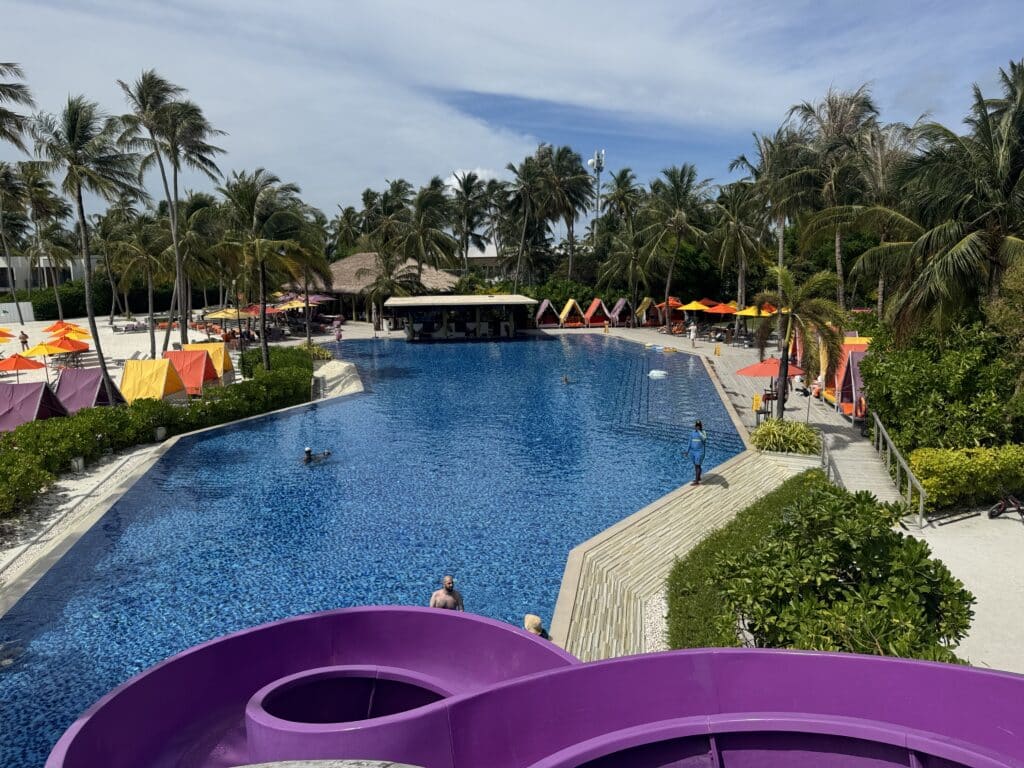 How to Choose a Maldives Resort: The Complete Decision Guide 6 large resort pool with water slide at Hard Rock Hotel Maldives surrounded by colourful cabanas and palm trees