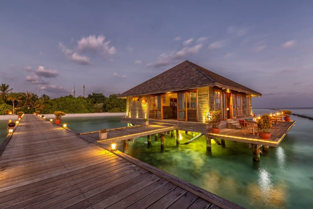 Aqua restaurant at Komandoo Island Resort Maldives illuminated at dusk over the lagoon