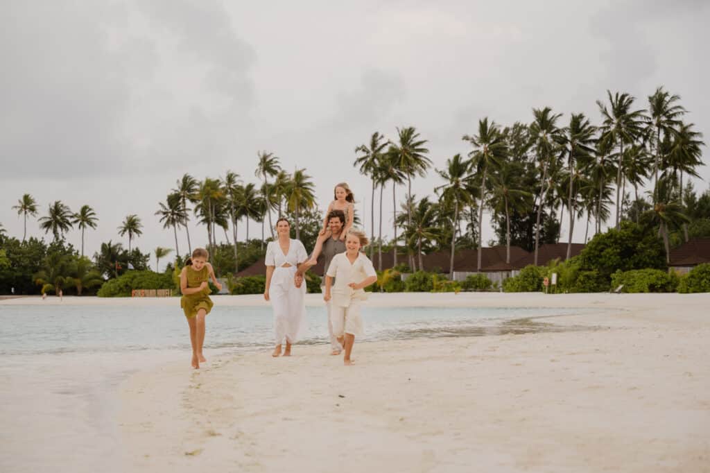 Maldive con bambini: resort o isole locali — Qual è la scelta giusta per la tua famiglia? 29 Famiglia con bambini che cammina su una spiaggia di sabbia bianca al resort Siyam World Maldives
