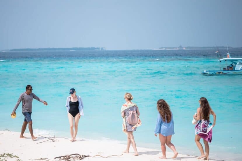 Maafushi Maldives: The Complete Budget Travel Guide to the Most Popular Local Island 14 people in swimwear and cover-ups on a white sand beach beside turquoise water