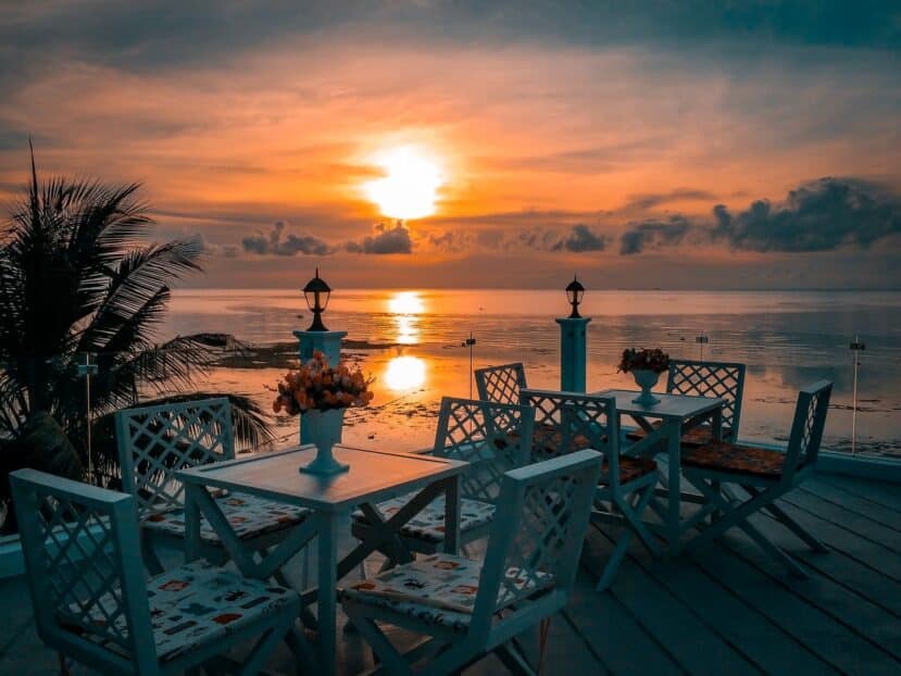 Maafushi Maldives: The Complete Budget Travel Guide to the Most Popular Local Island 13 white tables and chairs on a seaside restaurant deck overlooking the ocean at sunset