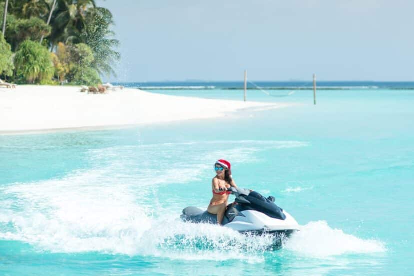 Maafushi Maldives: The Complete Budget Travel Guide to the Most Popular Local Island 12 person riding a jet ski across turquoise water beside a white sand beach