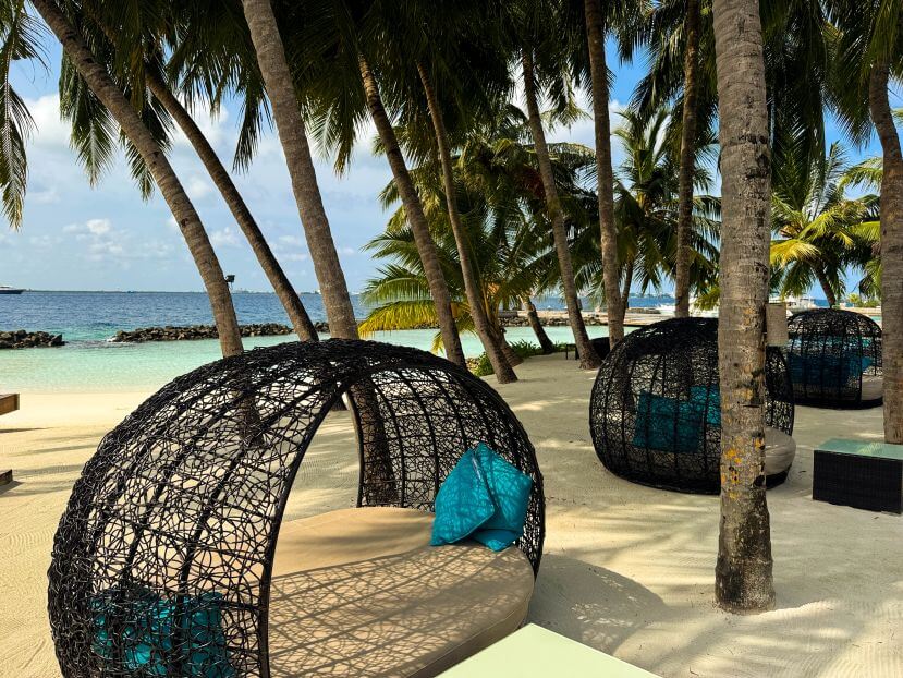 I migliori resort alle Maldive per chi visita per la prima volta: 10 isole che rendono tutto più semplice 2 lettini a forma di uovo intrecciato sulla spiaggia del Kurumba Maldives sotto le palme con laguna turchese