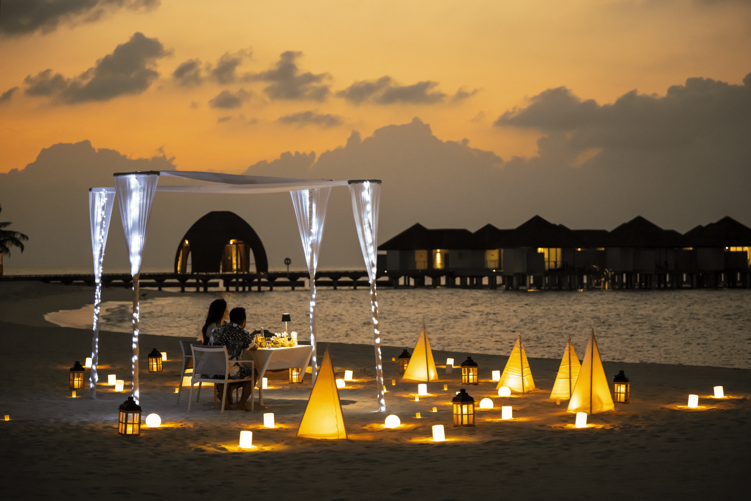 Los mejores resorts de Maldivas con mejor relación calidad-precio: 10 islas privadas que superan su precio 21 cena a la luz de las velas en la playa al atardecer con copas de champán en el resort Outrigger Maldives