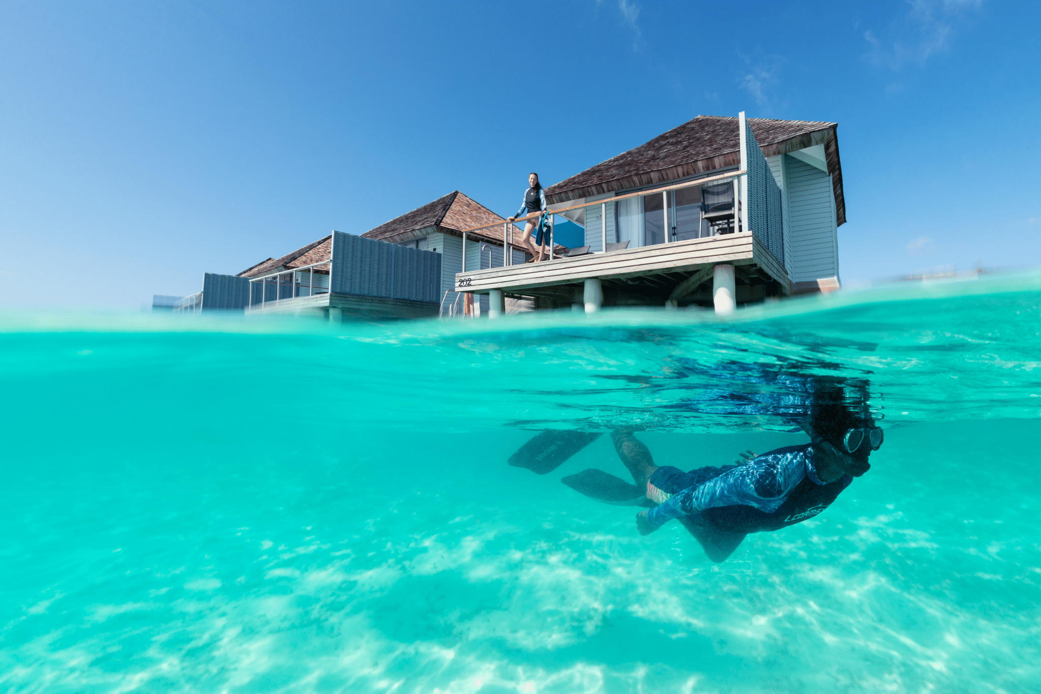 Los mejores resorts de Maldivas con mejor relación calidad-precio: 10 islas privadas que superan su precio 22 persona practicando esnórquel bajo el agua cerca de una villa sobre el agua en el resort Outrigger Maldives en una laguna turquesa