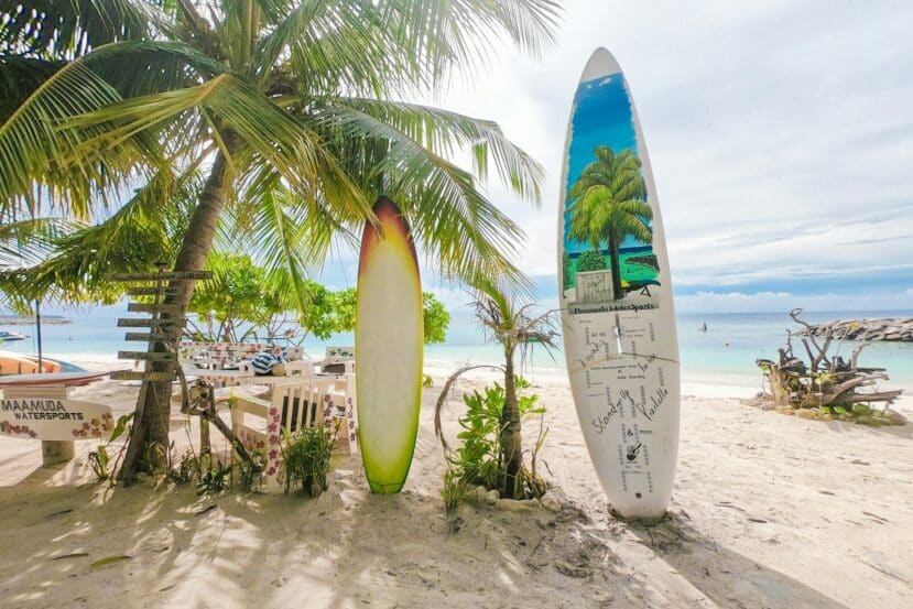 Maafushi Maldives: The Complete Budget Travel Guide to the Most Popular Local Island 2 decorated surfboards standing in the sand under a palm on Maafushi's bikini beach